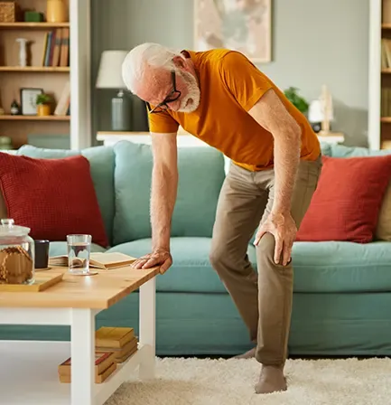 A man bending forward with one hand on his knee beside a sofa