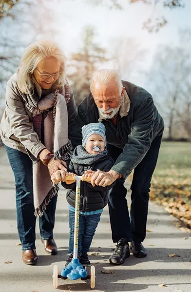 Grandparents helping a toddler ride a scooter