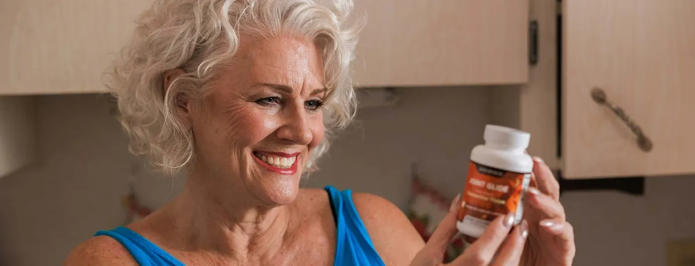 A woman smiling while holding a Joint Glide bottle at home