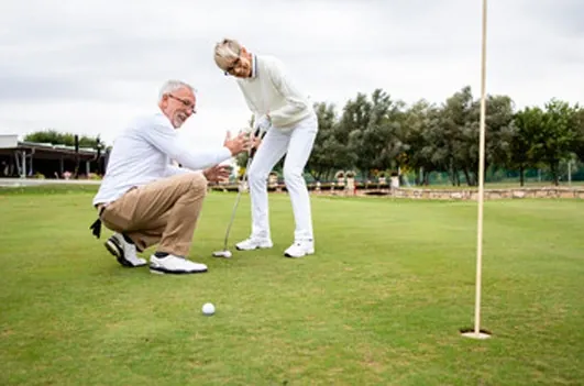 Two older men on a golf course, one mid-swing